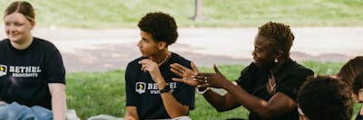 Students and a faculty member engage in discussion while seated in a circle on the grass.