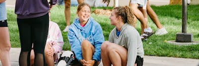 Students in sweatshirts relax and laugh together on the grass outside.
