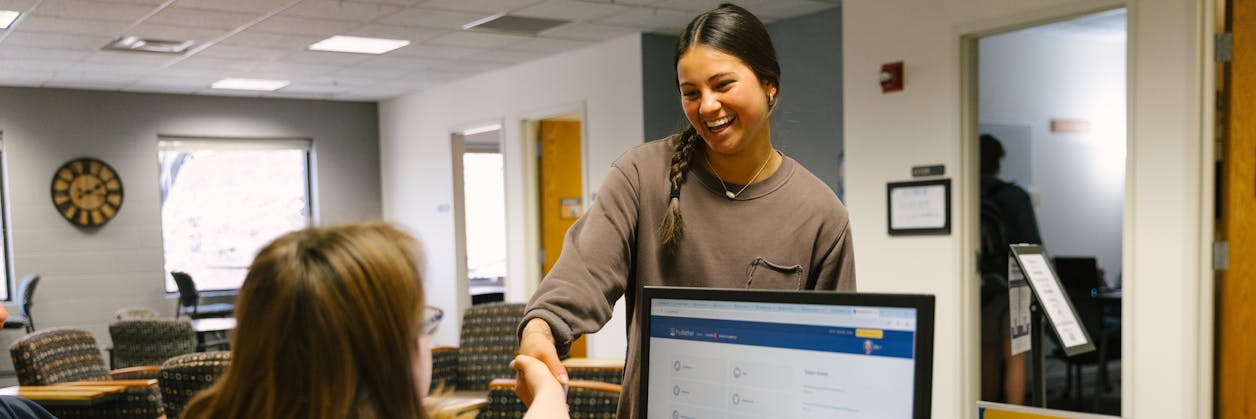 Smiling student gets help at a campus desk with a computer in the foreground.