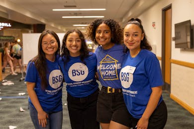 Four students in BSG and Welcome Week shirts smile and pose together during a campus event.