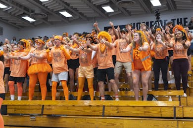 Students in orange cheer and chant from bleachers during a Nelson Hall campus spirit event.