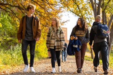 Students walk together along a tree-lined path covered in fall leaves at Bethel.