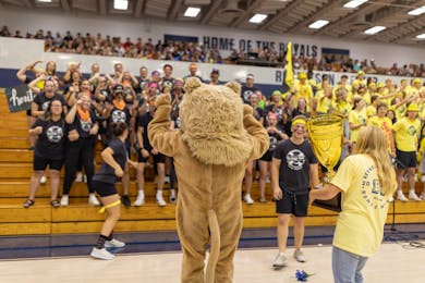 Students cheer in bleachers as the Bethel mascot and Homecoming host present a trophy on the gym floor.