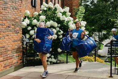 Two student leaders carry large blue bags during new student move-in at Bethel.